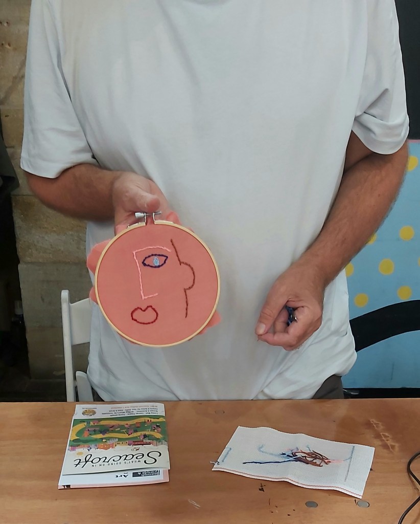 an image of a workshop participant holding up their embroidery work