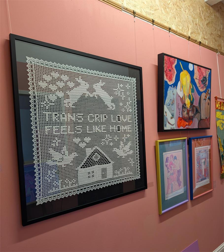 An image of the crochet piece 'Home' against a salmon pink wall, hung at exhibition. To the right are 3 smaller art works.