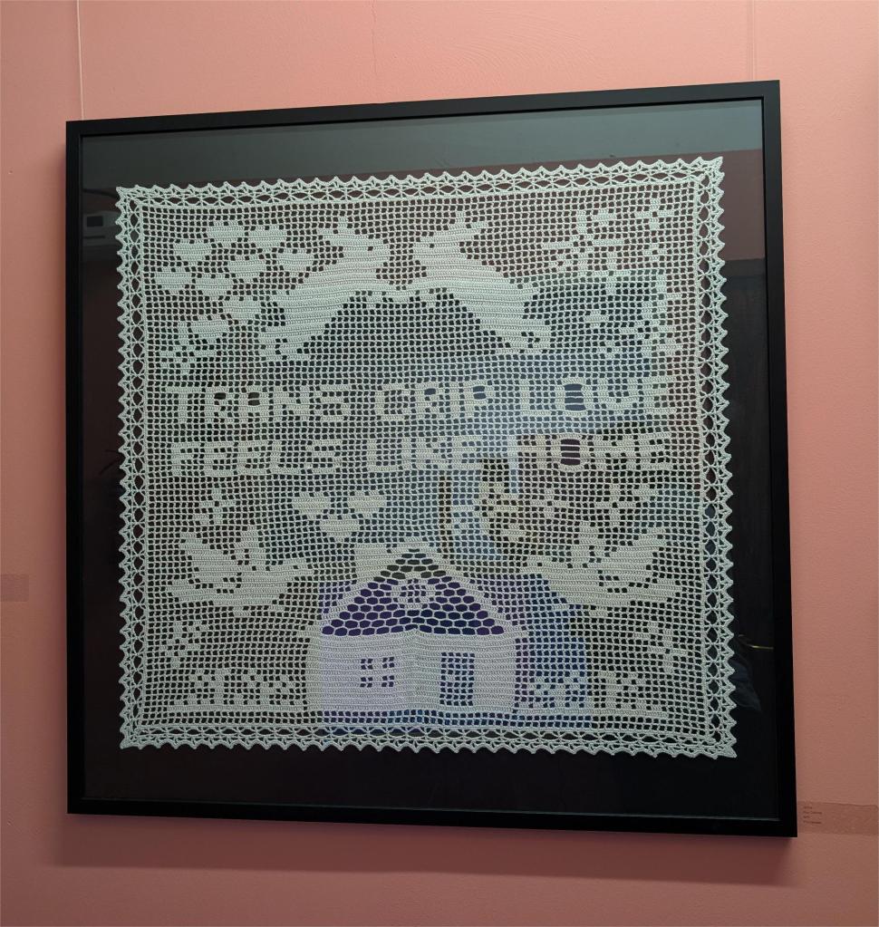 An image of the crochet piece 'Home' against a salmon pink wall, hung at exhibition