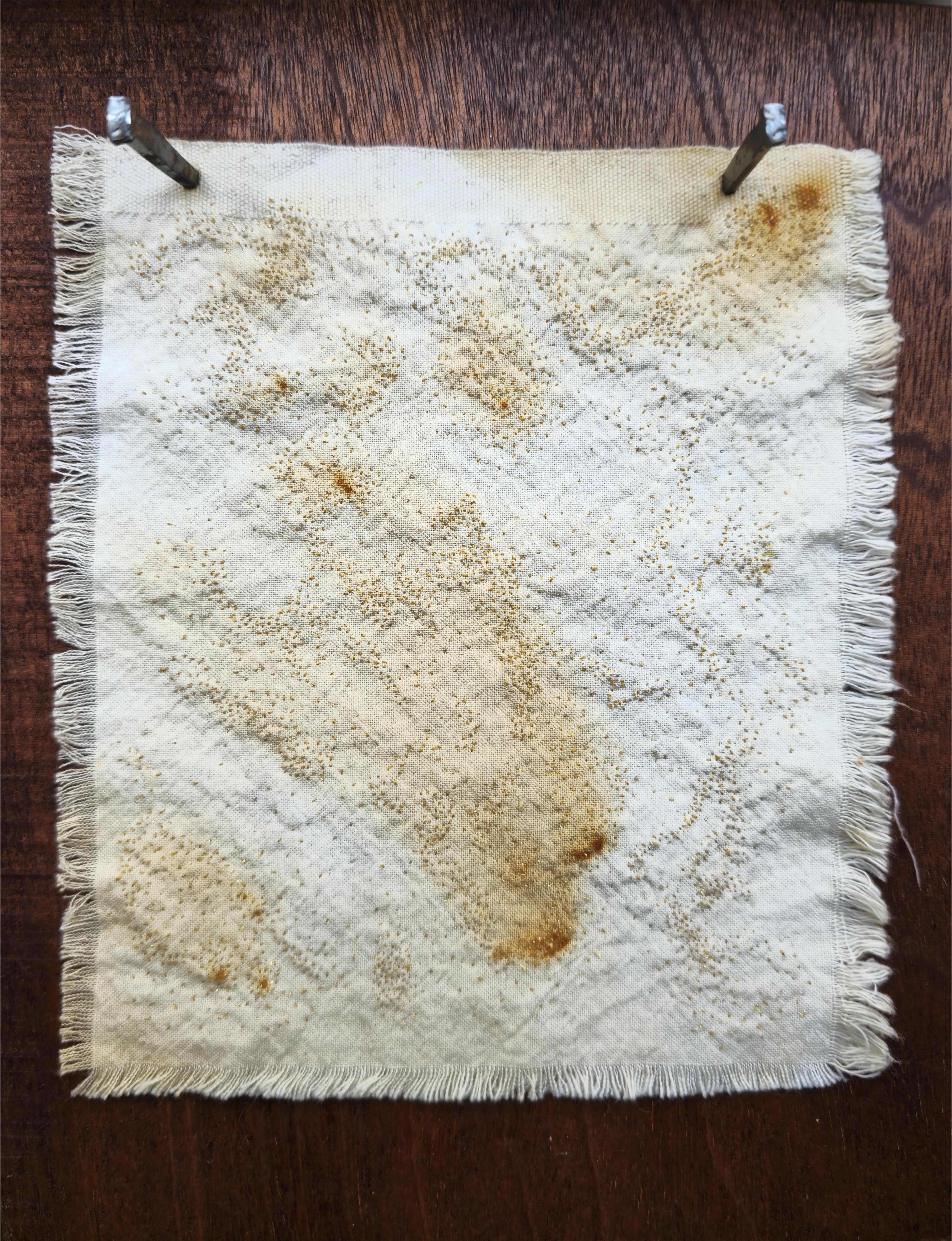 A piece of calico has been rust dyed, resulting in bursts of orange in varying hues across the fabric. Into this, tiny stitches in orange and gold have been made to resemble embers of a fire. The edges of the fabric have been left raw, and it has been hammered into a piece of mahogany coloured wood with antique nails.